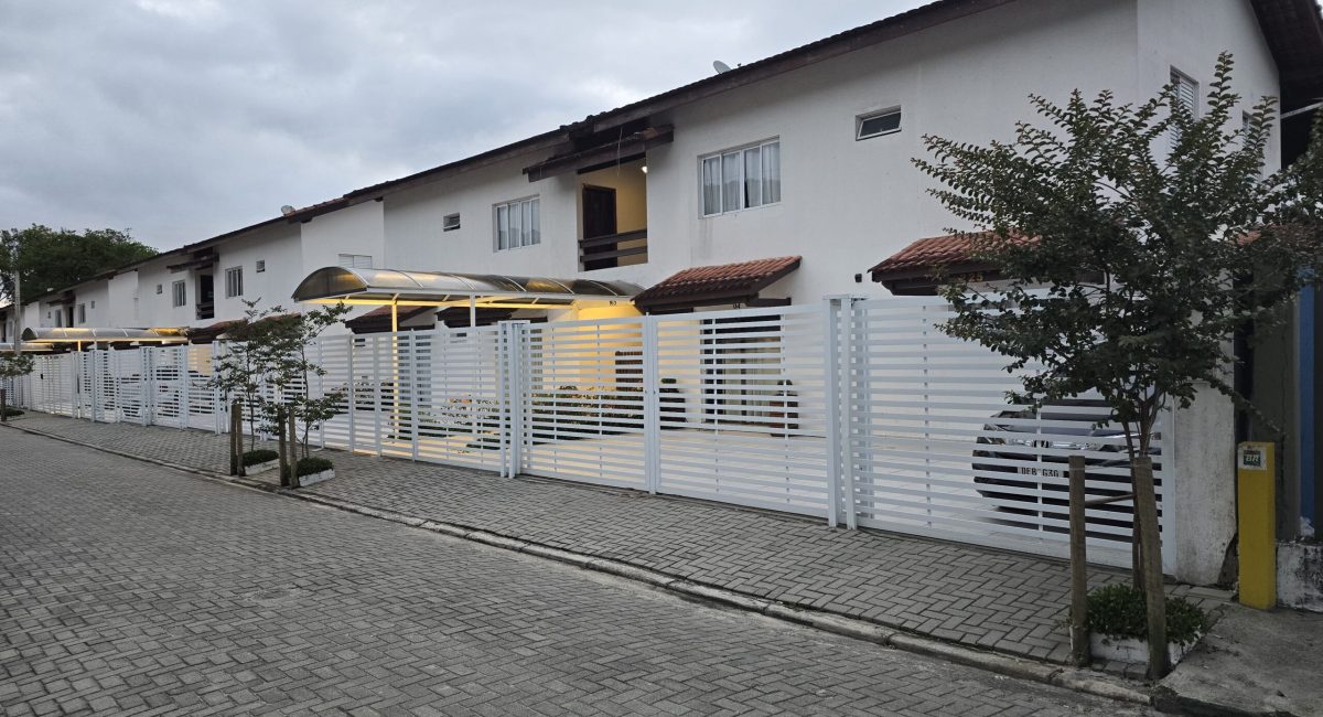 Fachada externa de casa de temporada em Juquehy em condomínio fechado com portão branco e calçada pavimentada.