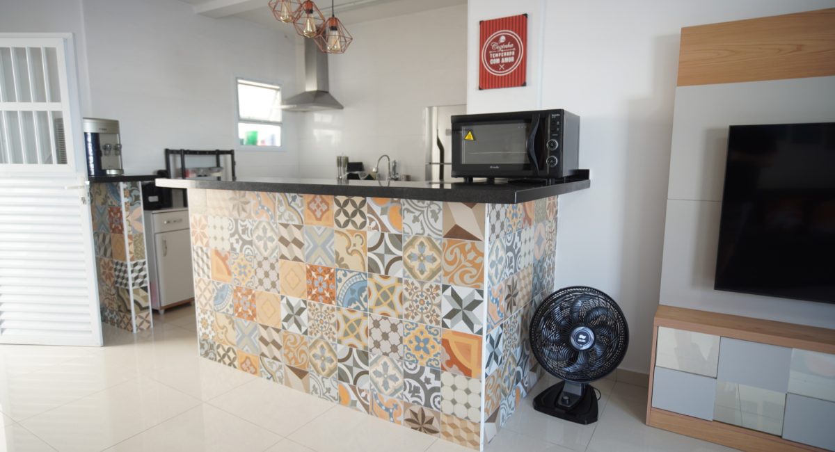 Vista da cozinha americana em casa de praia em Juquehy com bancada de ladrilhos hidráulicos, cooktop e forno elétrico.
