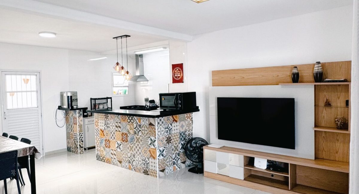 Sala de estar mobiliada de casa de praia em Juquehy com sofá cinza, TV de tela plana, ar-condicionado e Wi-Fi para home office.